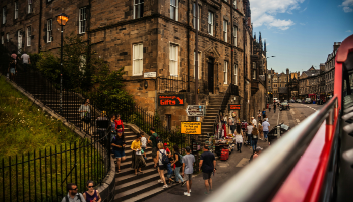 Street view from an Edinburgh open-top bus tour passing historic stone buildings and busy city streets.