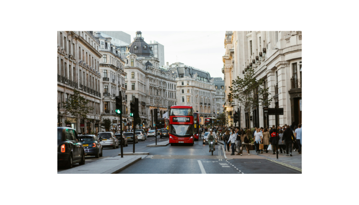 Red double-decker bus driving through a busy London street surrounded by historic buildings and pedestrians.