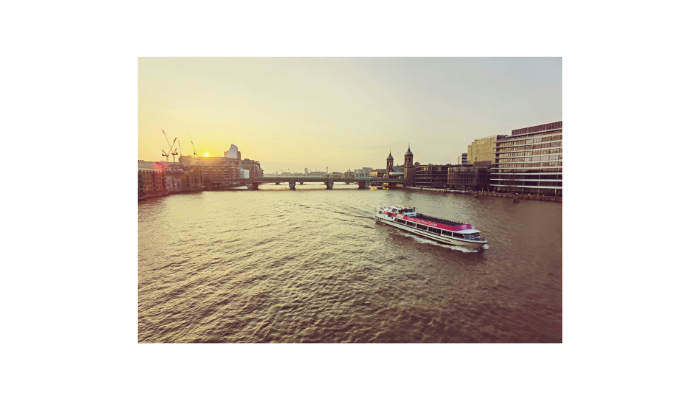 Sightseeing boat cruising along the River Thames during sunset with London skyline views in the background.