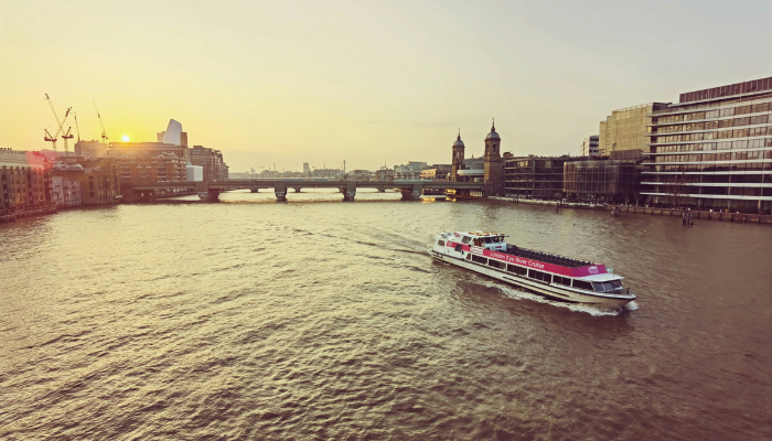 Sightseeing boat cruising along the River Thames during sunset with London skyline views in the background.