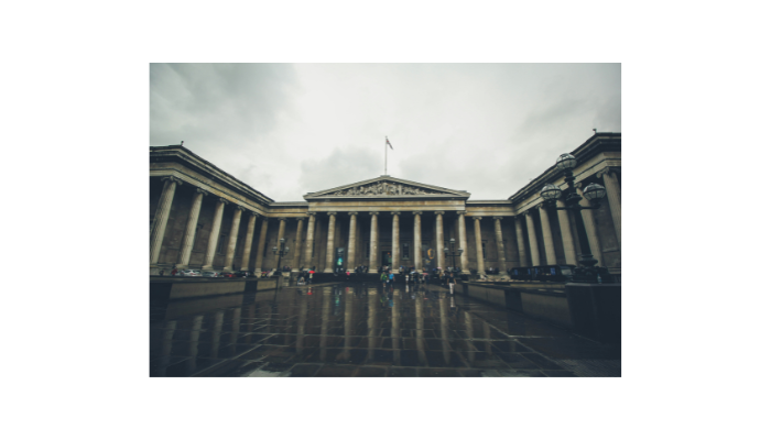 Front entrance of the British Museum in London on a rainy day with reflections on the ground.