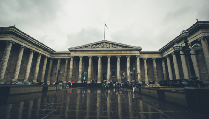 Front entrance of the British Museum in London on a rainy day with reflections on the ground.