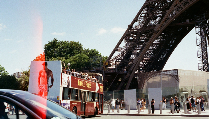 Red Paris hop-on hop-off sightseeing bus passing near the Eiffel Tower, showing a scenic way for tourists to explore Paris.
