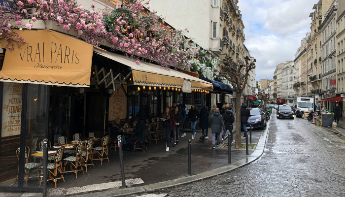 Charming Montmartre street in Paris with cafés and flower-covered storefronts, showing the city’s local neighborhood atmosphere.