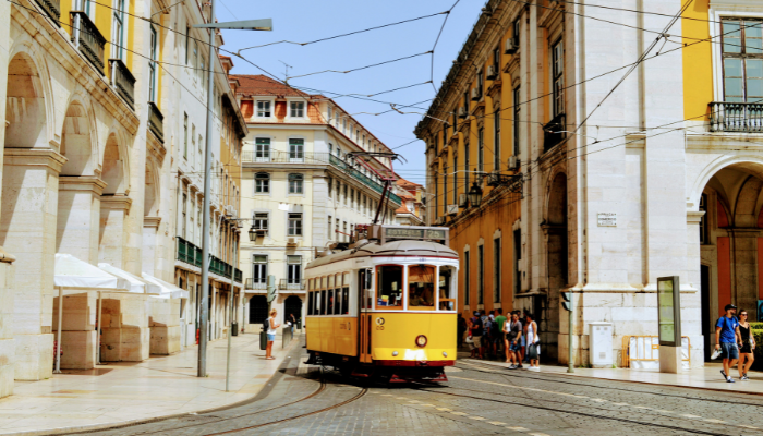 Yellow tram moving through Lisbon street with historic buildings and narrow lanes in Portugal.