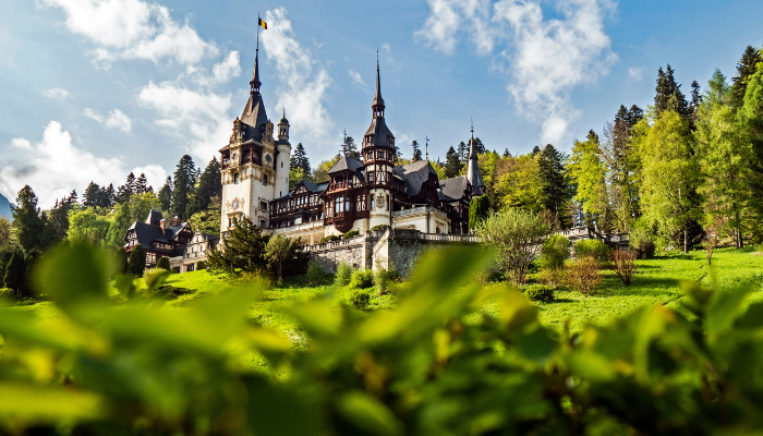 Peles Castle in Romania surrounded by forest and mountains with detailed European architecture.