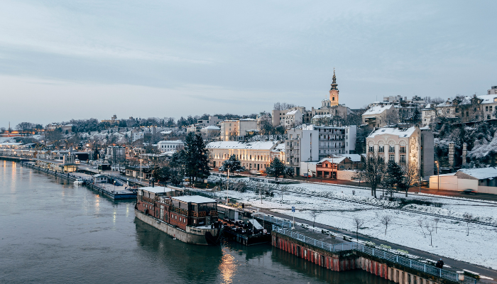 Snow-covered Belgrade riverside with Danube river, historic buildings, and winter cityscape.