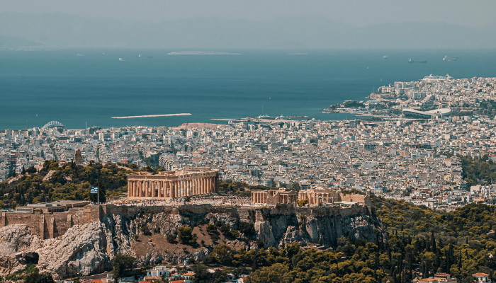 Panoramic view of the Acropolis and Athens cityscape with the Aegean Sea visible in the background.