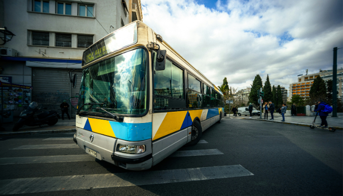 Public bus travelling through a city street in Athens, illustrating local transportation options for visitors.