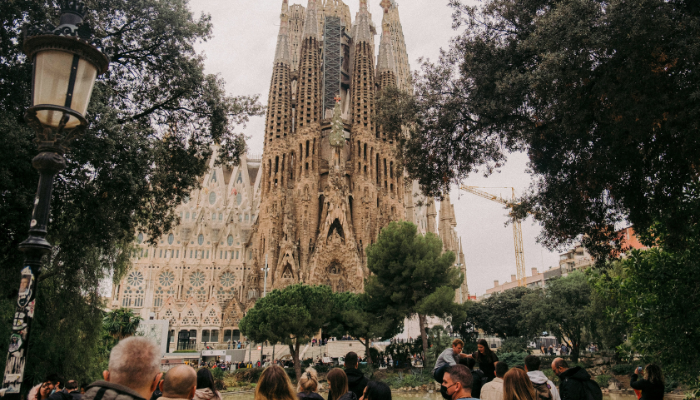 Visitors gathered in front of Sagrada Família in Barcelona, admiring Antoni Gaudí's world-famous basilica from a nearby park.
