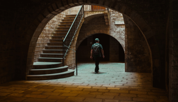 A traveler walking through a historic stone passageway in Barcelona's Gothic Quarter, surrounded by medieval architecture.