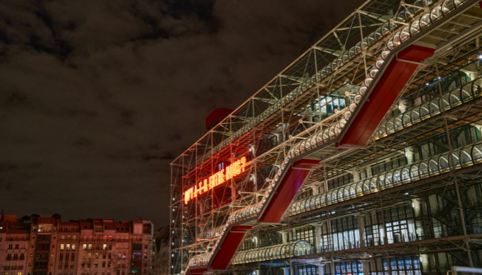 Exterior view of the Centre Pompidou in Paris at night, showcasing its iconic inside-out architecture and colorful external escalators.