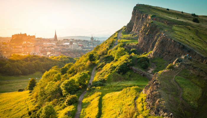 Sunlit hiking trail leading to Arthur's Seat with panoramic views over Edinburgh and the surrounding landscape.