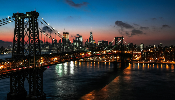 New York City skyline and illuminated bridge at sunset with reflections over the river