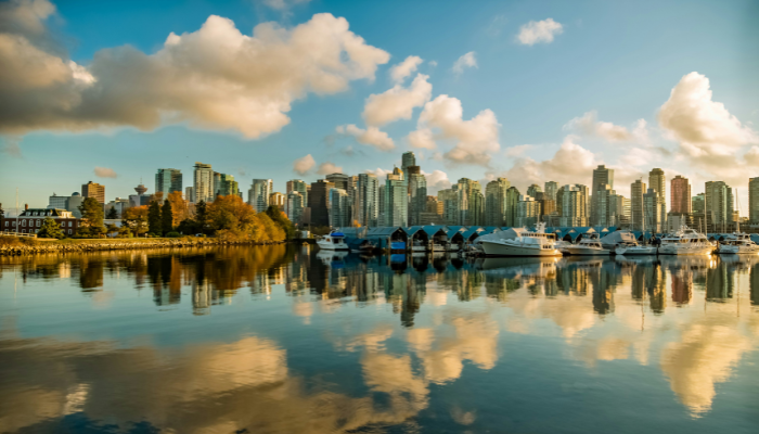 Vancouver waterfront skyline with boats calm water reflections and city buildings under soft clouds.