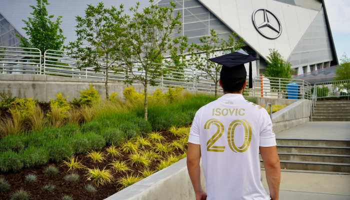 Football fan wearing a jersey walking near Mercedes Benz Stadium in Atlanta before a major match.