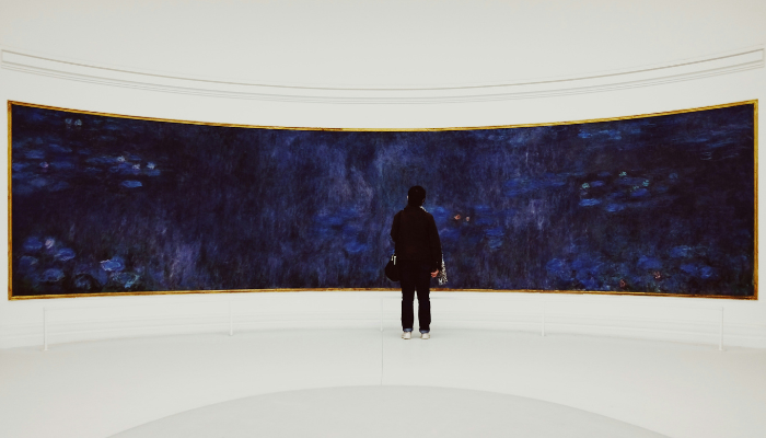 A visitor admiring Claude Monet's panoramic Water Lilies paintings inside the oval gallery at Musée de l'Orangerie in Paris.