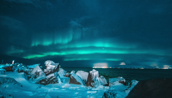 Northern Lights dancing over Iceland's snow-covered coastline at night, with green aurora illuminating the sky above rocky shores.