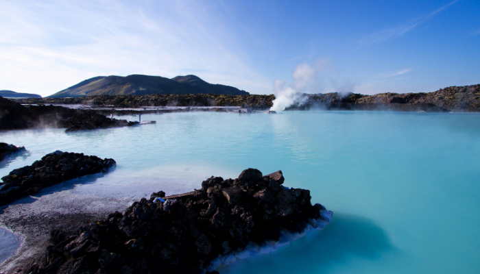 The Blue Lagoon in Iceland featuring milky-blue geothermal waters surrounded by black lava rocks and rising steam under a clear sky.