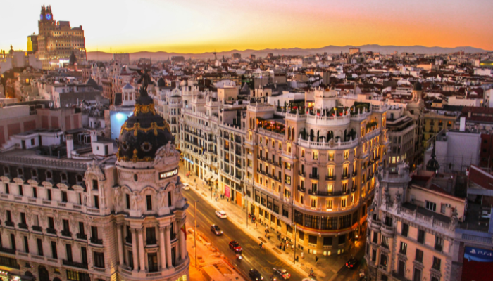 Evening skyline of Madrid's Gran Vía with illuminated historic buildings and bustling streets.