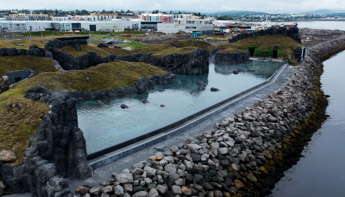 Aerial view of Sky Lagoon in Reykjavík showing its oceanfront geothermal pools, lava rock formations, and infinity-edge design overlooking the coastline.