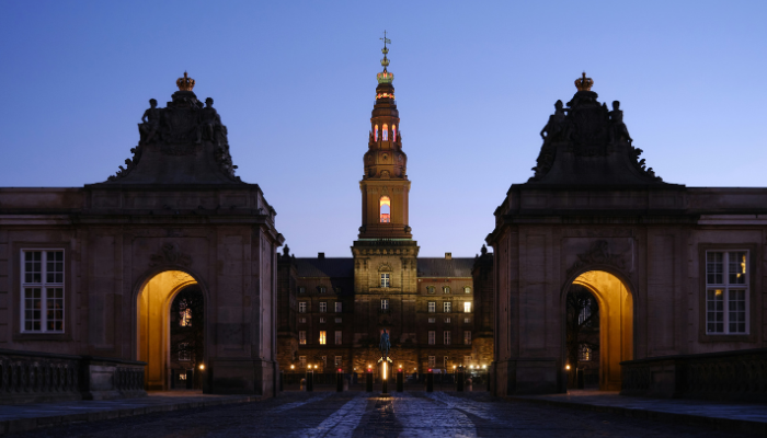 Christiansborg Palace in Copenhagen illuminated at dusk, viewed through the palace entrance gates.