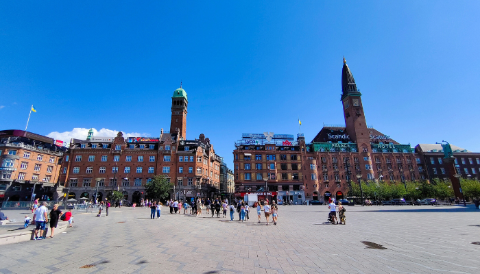 Copenhagen City Hall Square with historic buildings, busy pedestrian areas and the City Hall towers under a clear blue sky.