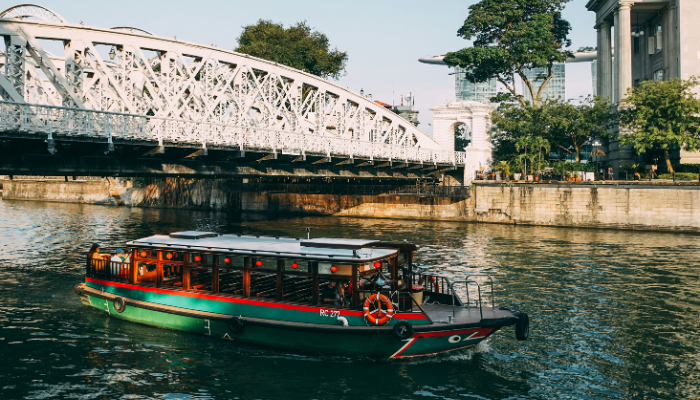 Singapore River cruise boat passing beneath a historic bridge near the waterfront.