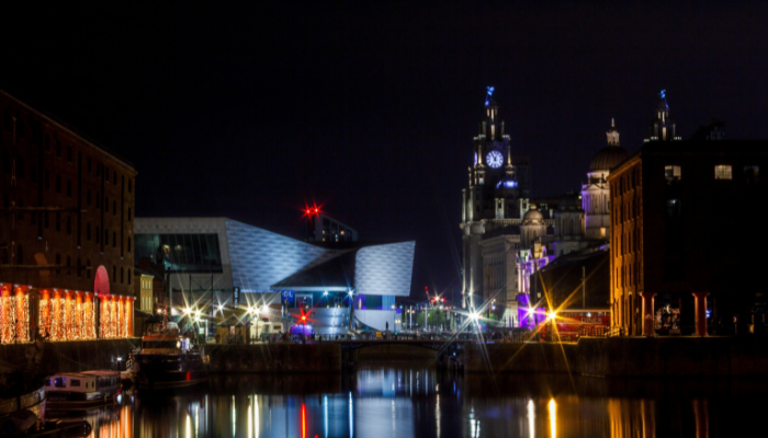 Liverpool waterfront at night with the Museum of Liverpool and historic buildings reflected in the water.