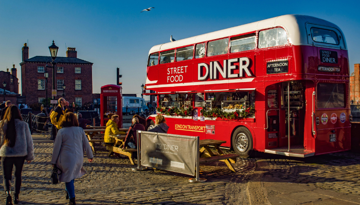 Red double-decker street food bus parked beside outdoor seating in Liverpool