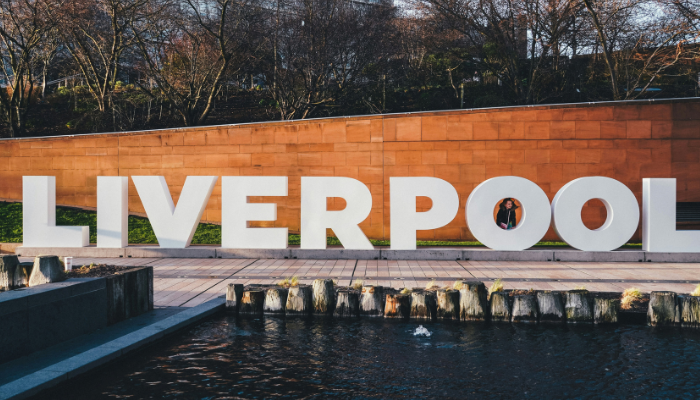 Large white Liverpool sign beside a waterfront pool surrounded by trees