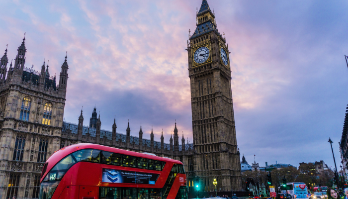Red London double-decker city bus passing Big Ben and the Houses of Parliament.