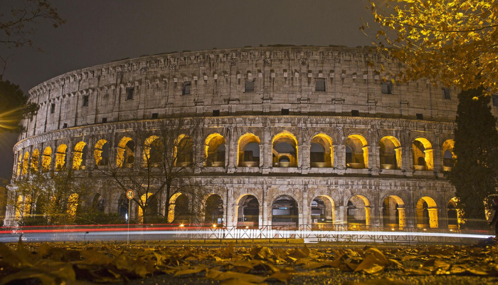 Rome’s illuminated Colosseum at night surrounded by autumn trees and historic streets