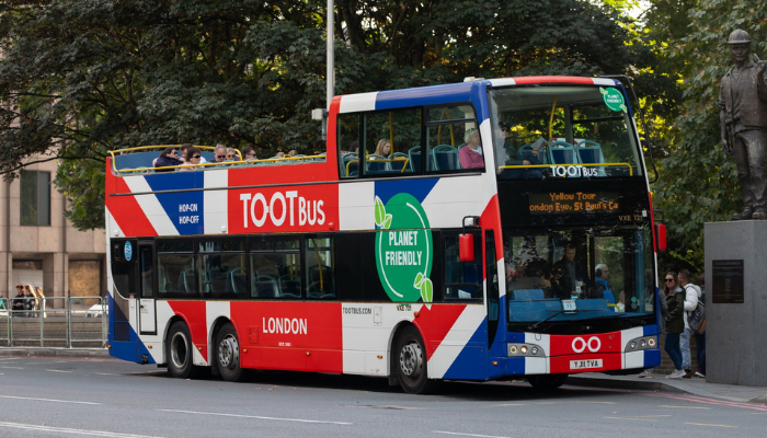 Tootbus open-top sightseeing bus on a London street near a statue.
