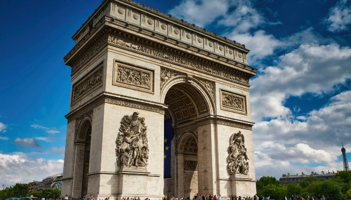 Arc de Triomphe in Paris with ornate stone sculptures and a blue sky