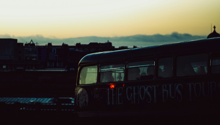 Dark Edinburgh ghost bus at dusk with the city skyline in the background